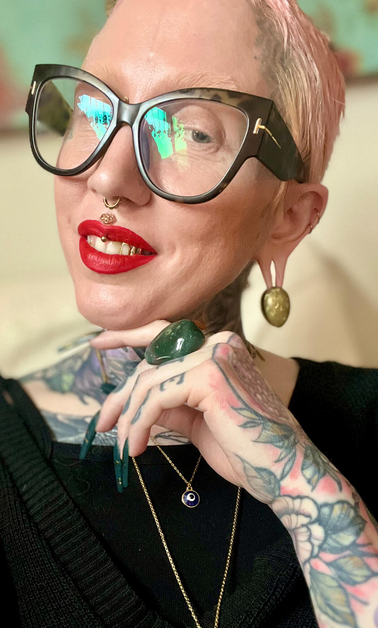 Photo of Lor Begent with cat eye glasses, piercings, jewelry, tattoos, and red lipstick.